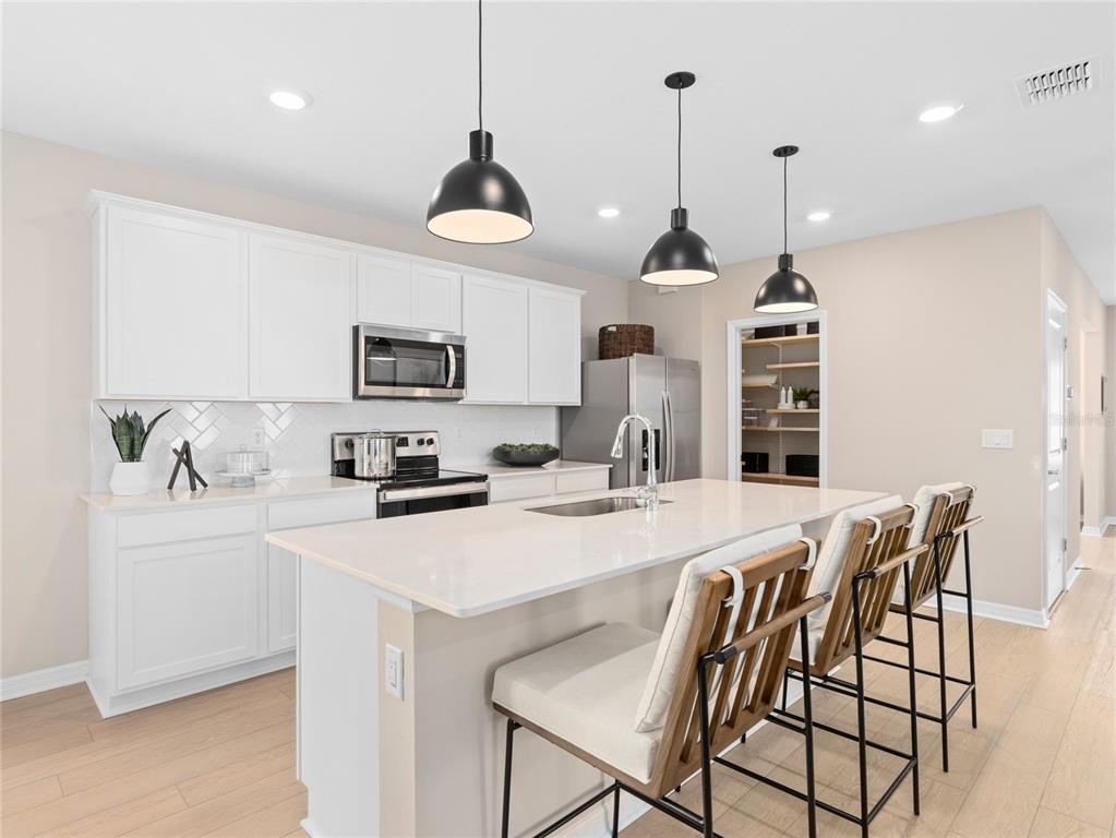 A modern kitchen features white cabinets, a quartz island with bar seating, and pendant lighting — 10710 LEAFY LAUREL STREET, ORLANDO, FL