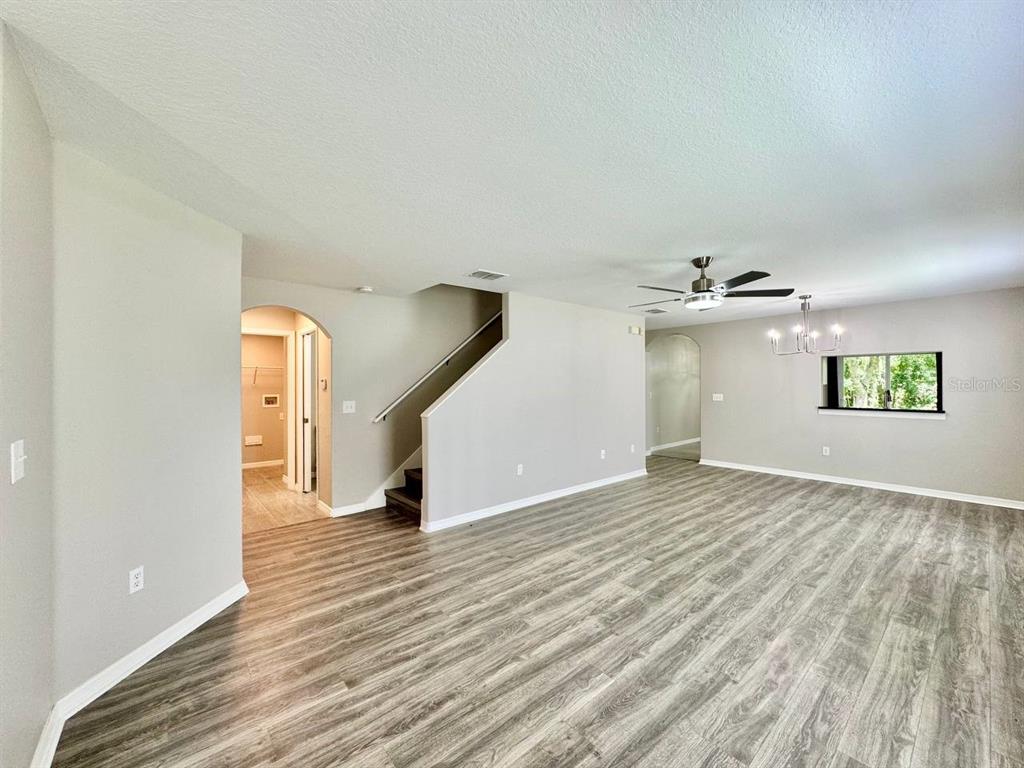 An open living area features wood-look flooring, a staircase, a ceiling fan, and a chandelier — 12534 CHENWOOD AVENUE, HUDSON, FL