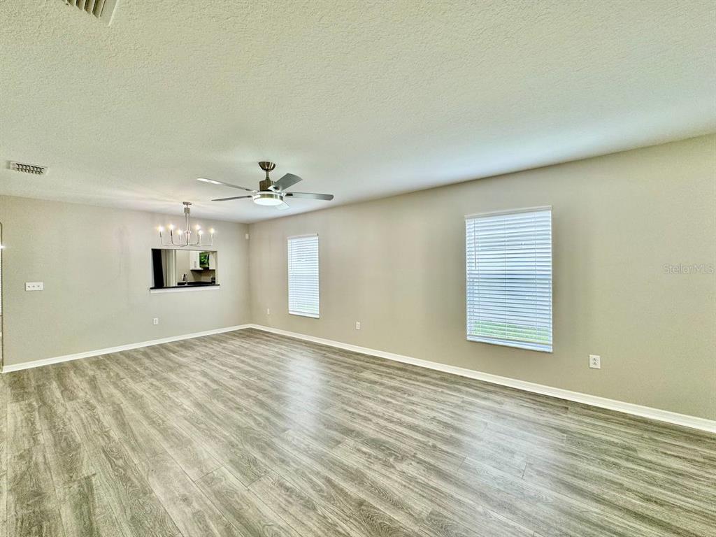 An empty living room features light gray wood-look flooring, beige walls, and a ceiling fan — 12534 CHENWOOD AVENUE, HUDSON, FL