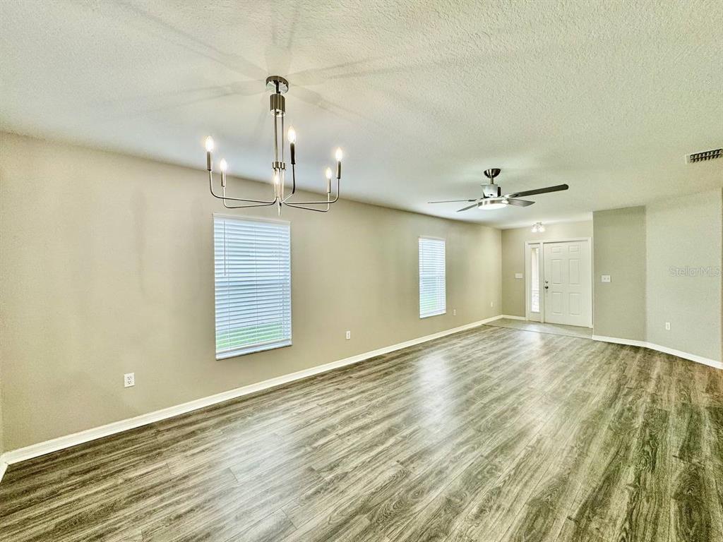 An empty room features wood-look flooring, a modern chandelier, a ceiling fan, and white blinds — 12534 CHENWOOD AVENUE, HUDSON, FL