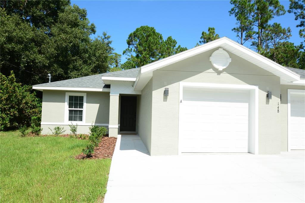 A light-colored single-story house features a white garage door and a front entrance walkway — 148 SECRETARY TRAIL UNIT A/B, PALM COAST, FL