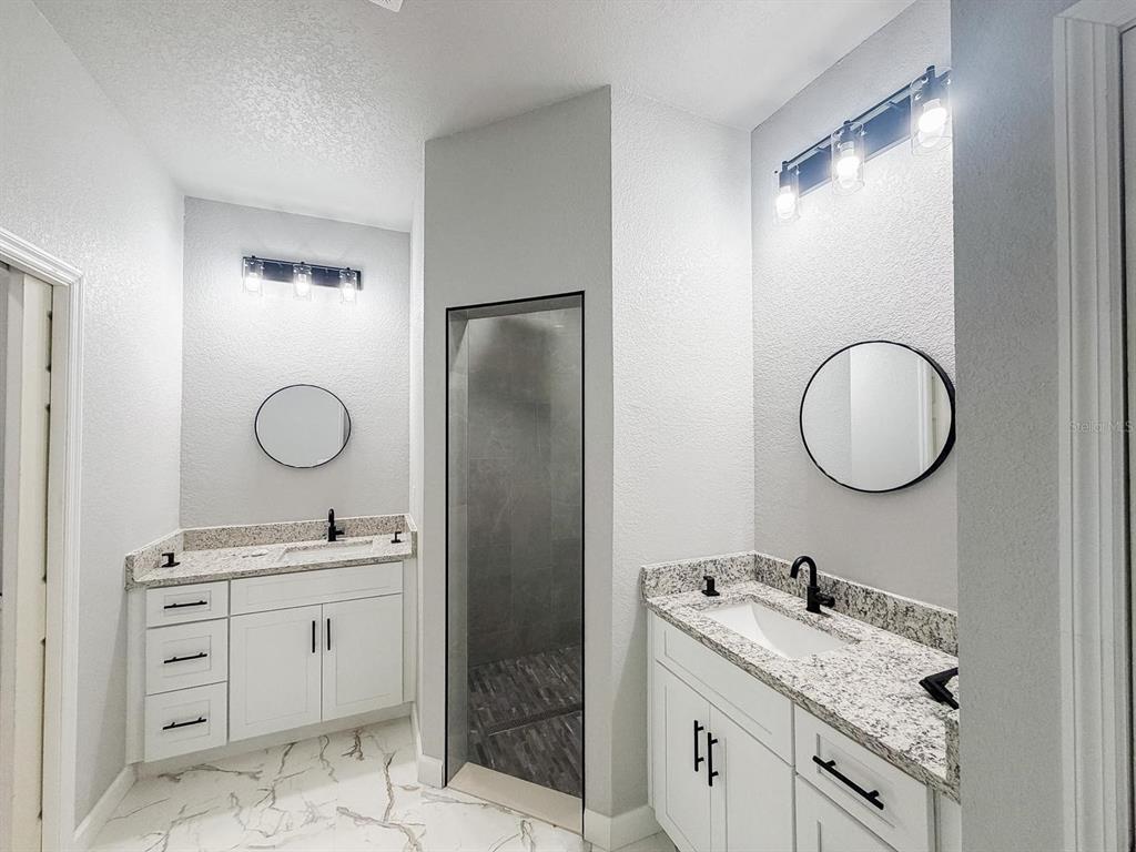 A bathroom features two white vanities with granite countertops, round mirrors, and a walk-in shower — 4200 LEAF ROAD, SEBRING, FL