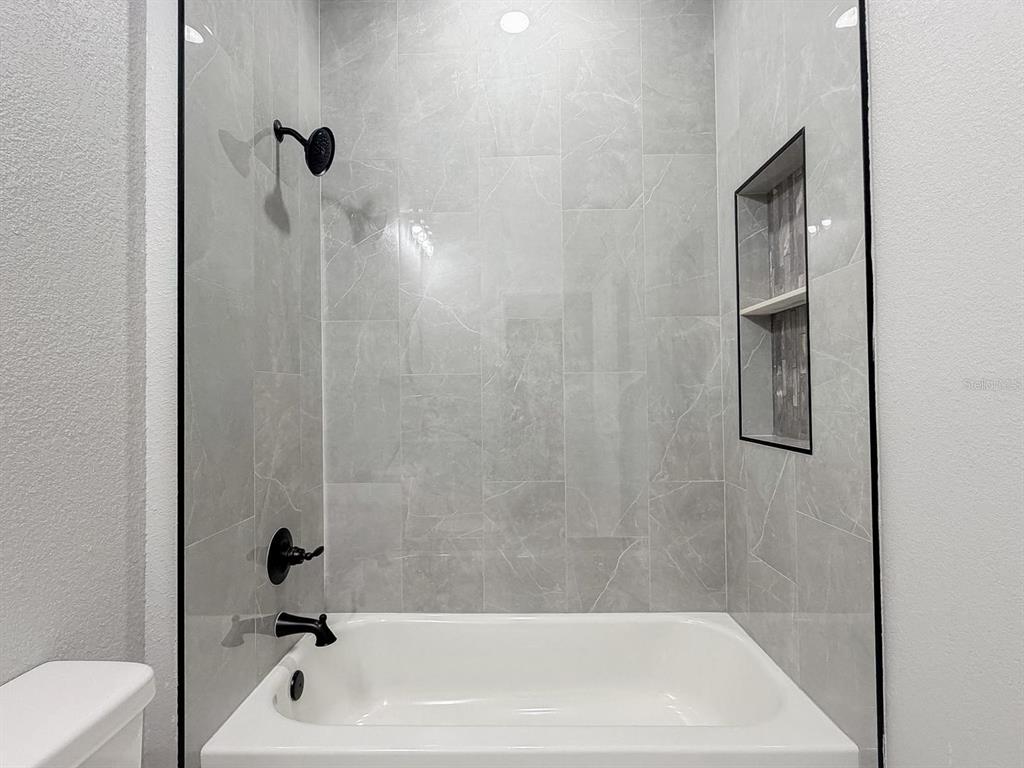 A bathtub with a shower head and a tiled wall niche in a modern bathroom — 4200 LEAF ROAD, SEBRING, FL