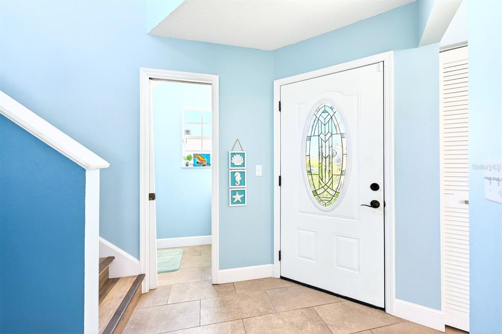 An entryway with light blue walls, tile flooring, a white front door, and a staircase — 1599 PGA BOULEVARD, MELBOURNE, FL