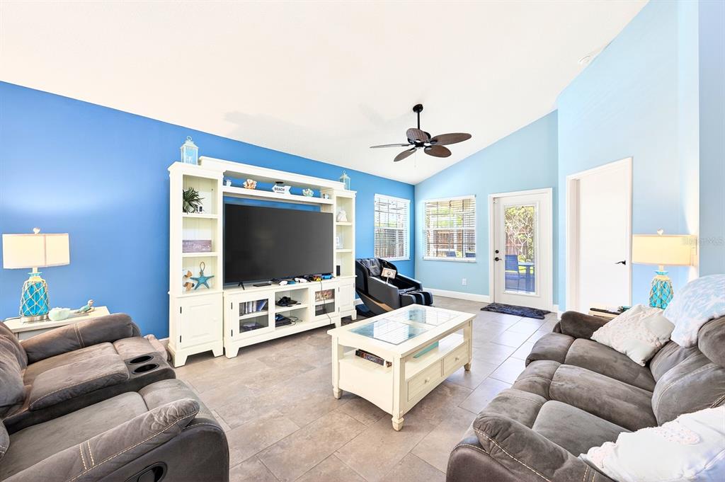 A living room with blue walls, a white entertainment center, two gray sofas, and tile flooring — 1599 PGA BOULEVARD, MELBOURNE, FL