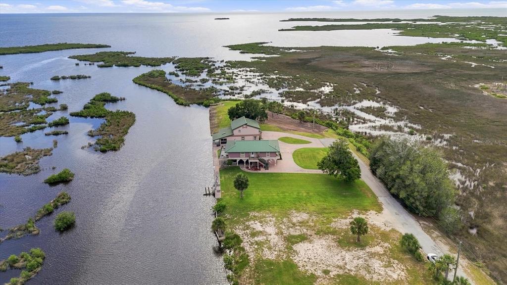 An aerial view shows a house with a green roof situated along a coastal waterway — 3198 INDIAN GULF LANE, HERNANDO BEACH, FL