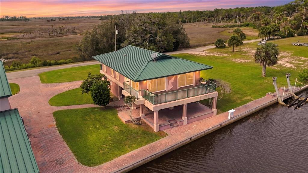 An elevated waterfront house with a green metal roof, a balcony, and a paved dock — 3198 INDIAN GULF LANE, HERNANDO BEACH, FL