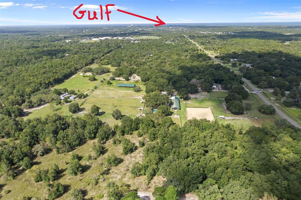 An aerial view shows a rural property with pastures, barns, and trees near the coast — 11046 KITTEN TRAIL, HUDSON, FL