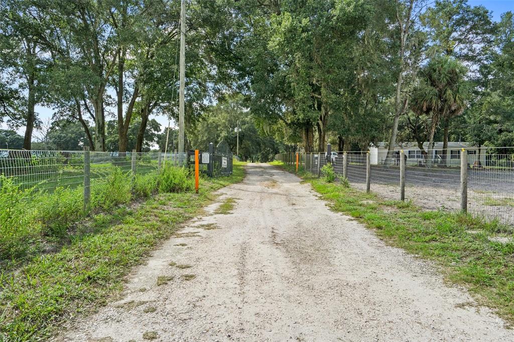 A dirt driveway leads toward a gated entrance flanked by wire fencing and mature trees — 11046 KITTEN TRAIL, HUDSON, FL