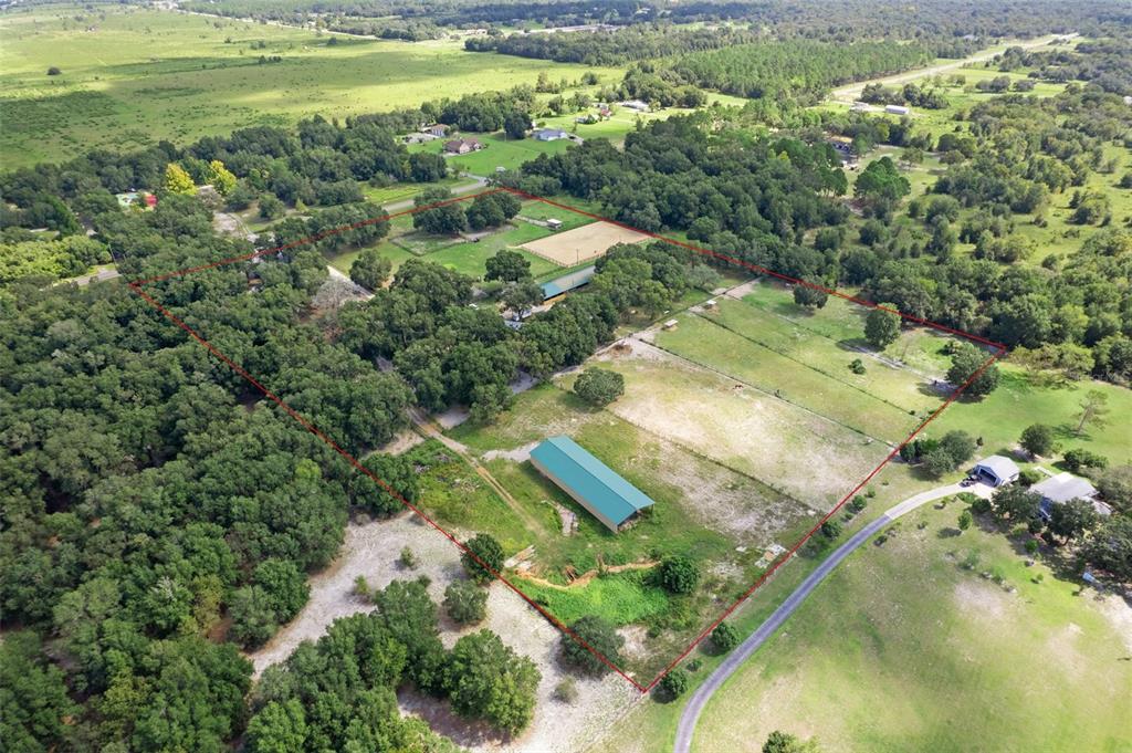 An aerial view shows a large, fenced rural property with a barn and riding arena — 11046 KITTEN TRAIL, HUDSON, FL