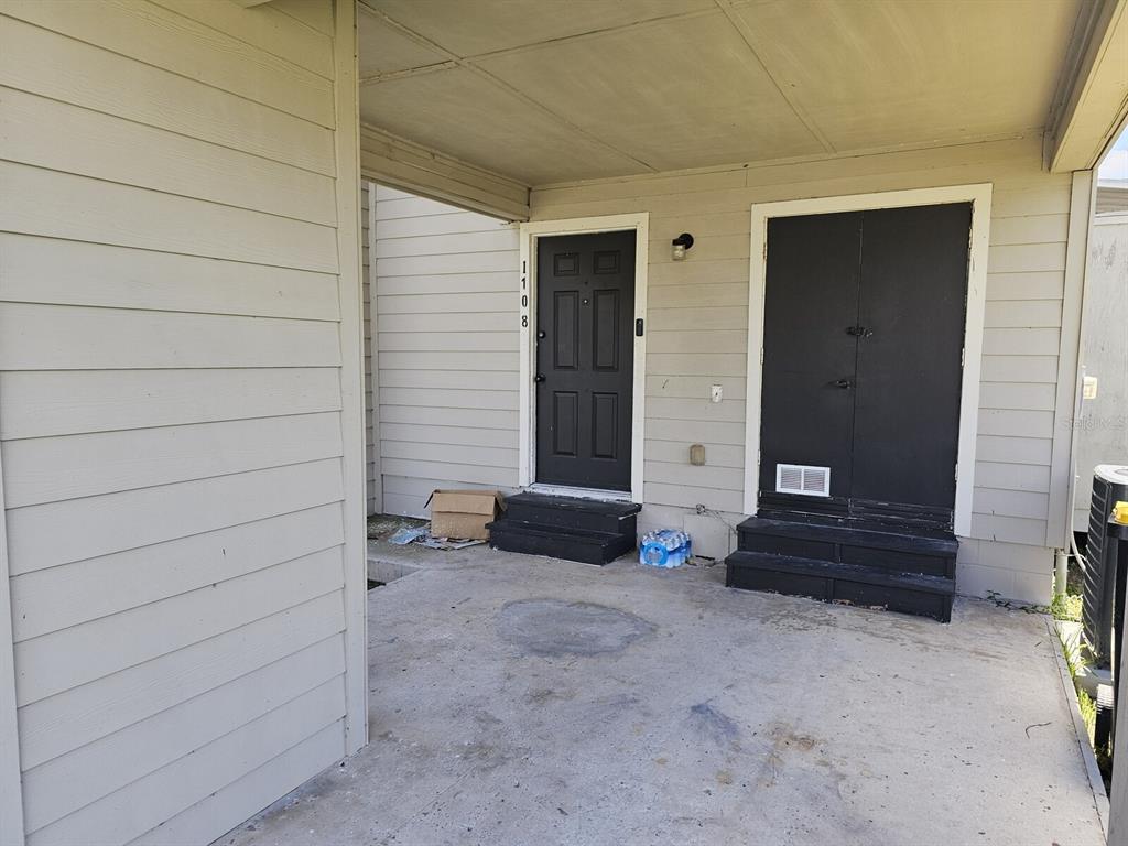 A covered concrete patio features two black doors with small steps leading to each entrance — 1106-1108 COUNTRY CLUB LANE, LAKELAND, FL