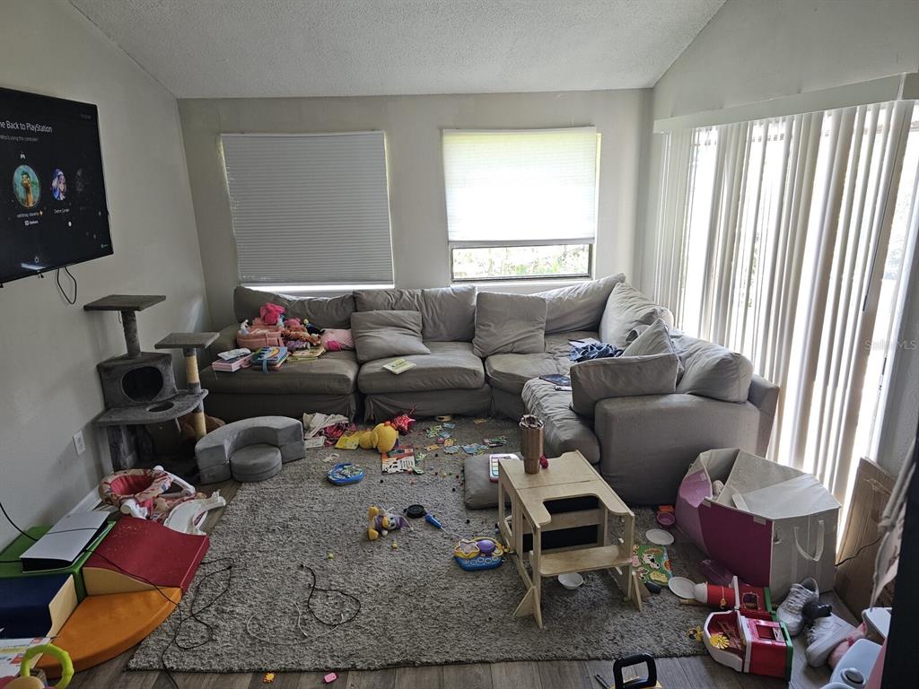 A living room with a large sectional sofa, a gray area rug, and scattered children's toys — 1106-1108 COUNTRY CLUB LANE, LAKELAND, FL