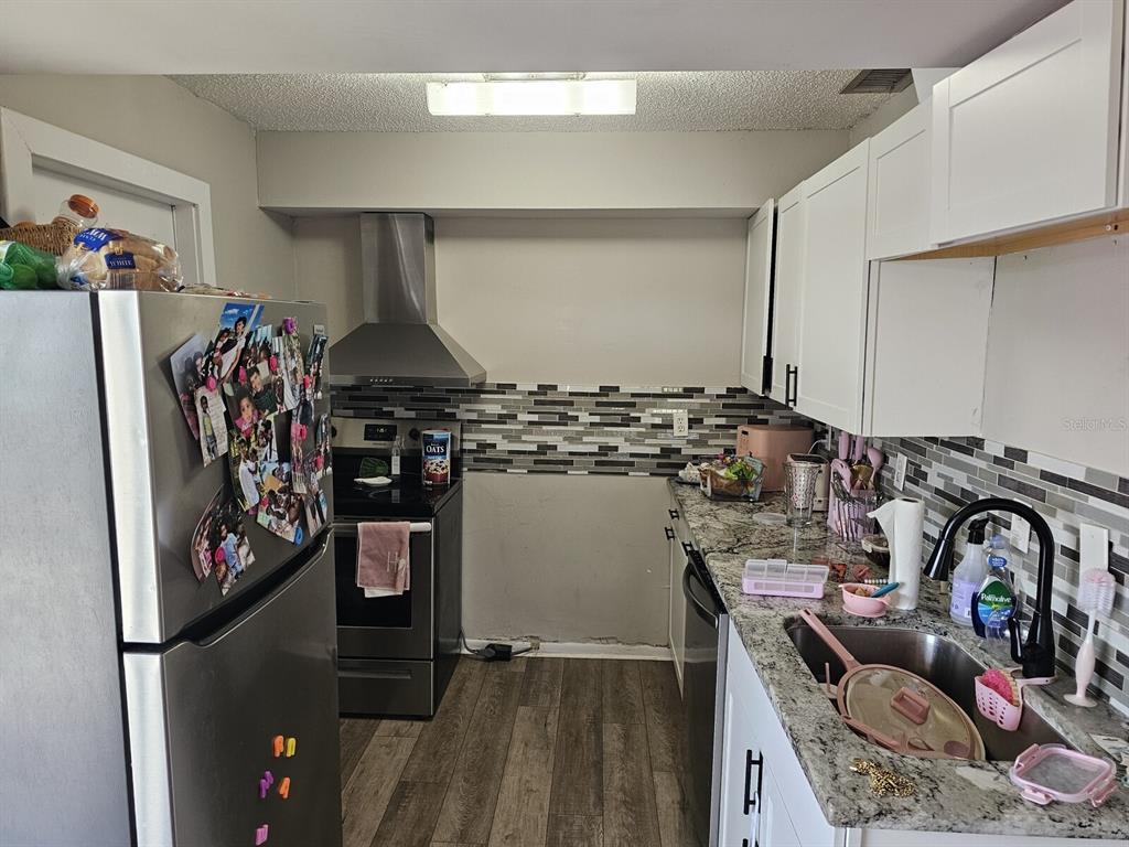 A kitchen features stainless steel appliances, white cabinets, granite countertops, and a tiled backsplash — 1106-1108 COUNTRY CLUB LANE, LAKELAND, FL