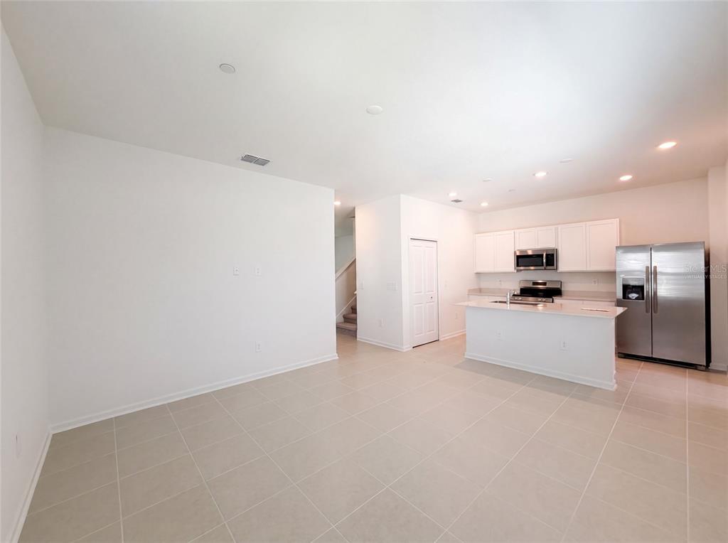 An open-concept kitchen and living area with white cabinets, stainless steel appliances, and tile flooring — 2172 RIDER RAIN LANE, APOPKA, FL