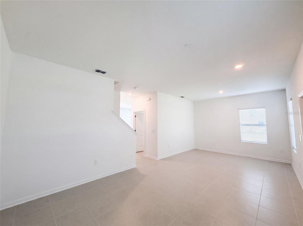 An empty room with white walls, light tile flooring, recessed lighting, and a staircase — 2172 RIDER RAIN LANE, APOPKA, FL