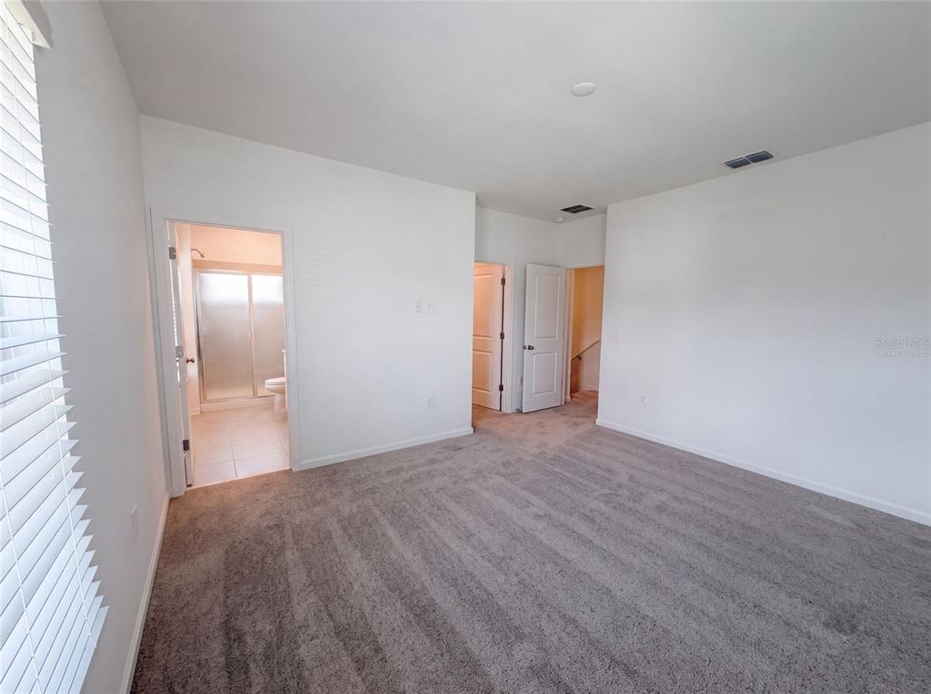 An empty bedroom with gray carpet, white walls, and doorways leading to a bathroom and hallway — 2172 RIDER RAIN LANE, APOPKA, FL