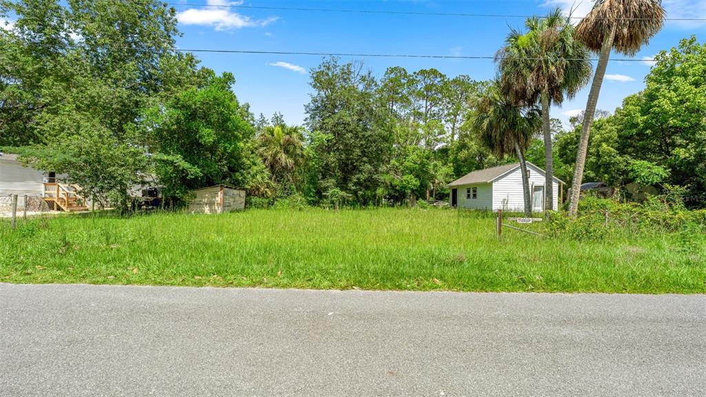 A grassy vacant lot sits between two small white buildings under a blue sky — 10085 PLUM STREET, HAMPTON, FL