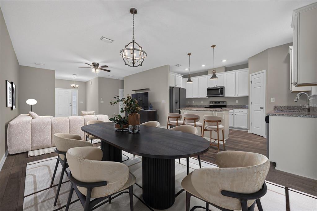 An open-concept dining area features a dark oval table, beige chairs, and a modern kitchen — 93 BELLA VITA WAY, ORMOND BEACH, FL