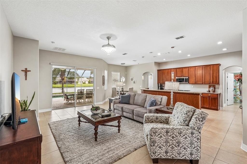 An open-concept living room features tile floors, a gray sofa, and a kitchen with wood cabinets — 5319 120TH AVENUE E, PARRISH, FL