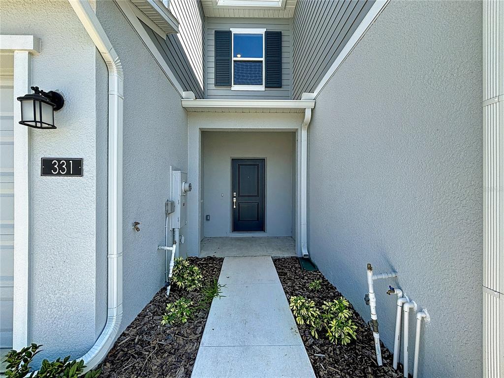 A concrete walkway leads to the dark front door of a gray stucco house — 331 SOL VISTA DRIVE, DUNDEE, FL