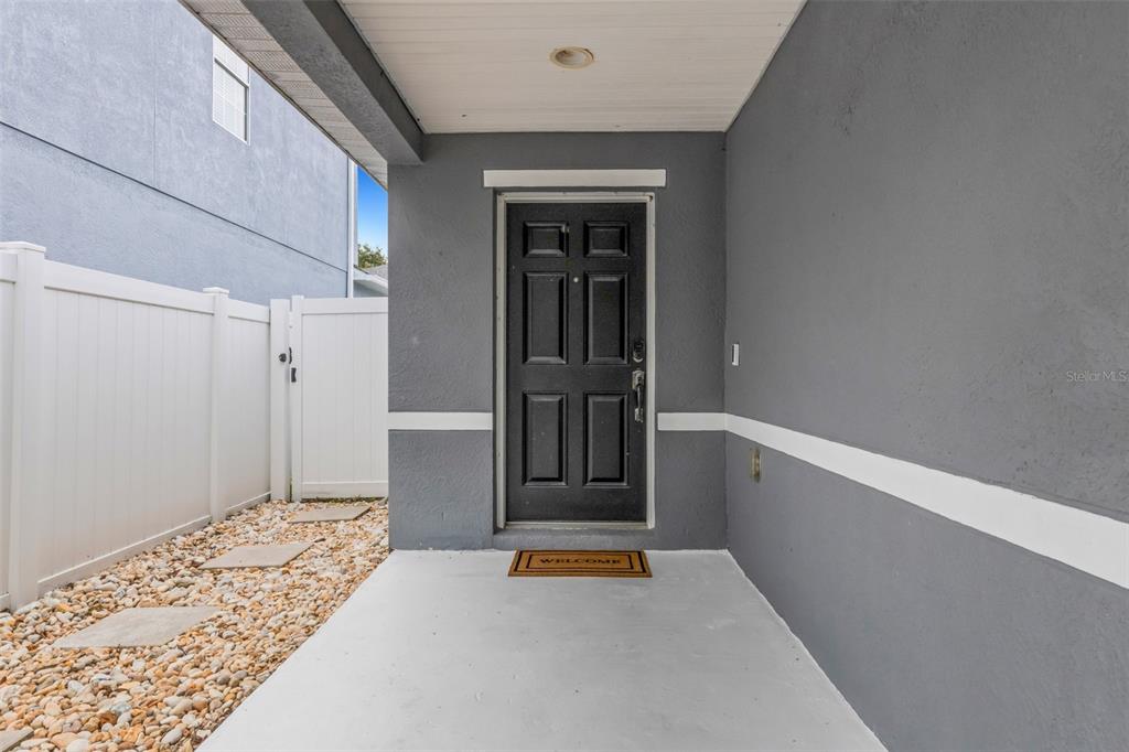 A covered concrete porch leads to a black front door with a white vinyl fence — 11136 GOLDEN SILENCE DRIVE, RIVERVIEW, FL