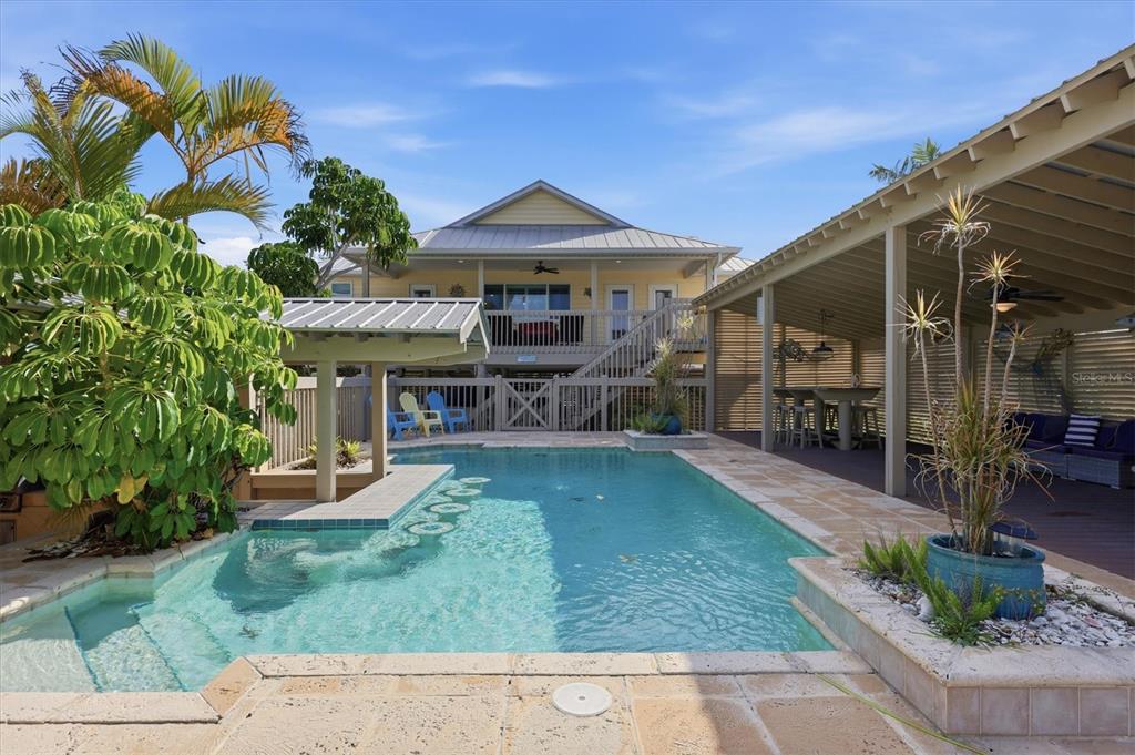 A backyard swimming pool with a swim-up bar sits in front of a raised house — 97 KETTLE HARBOR DRIVE, PLACIDA, FL