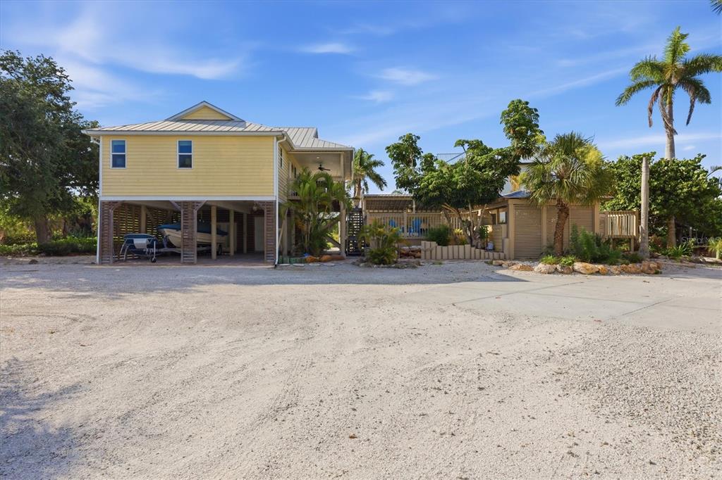 A yellow stilt house with a gravel driveway and a boat parked underneath — 97 KETTLE HARBOR DRIVE, PLACIDA, FL