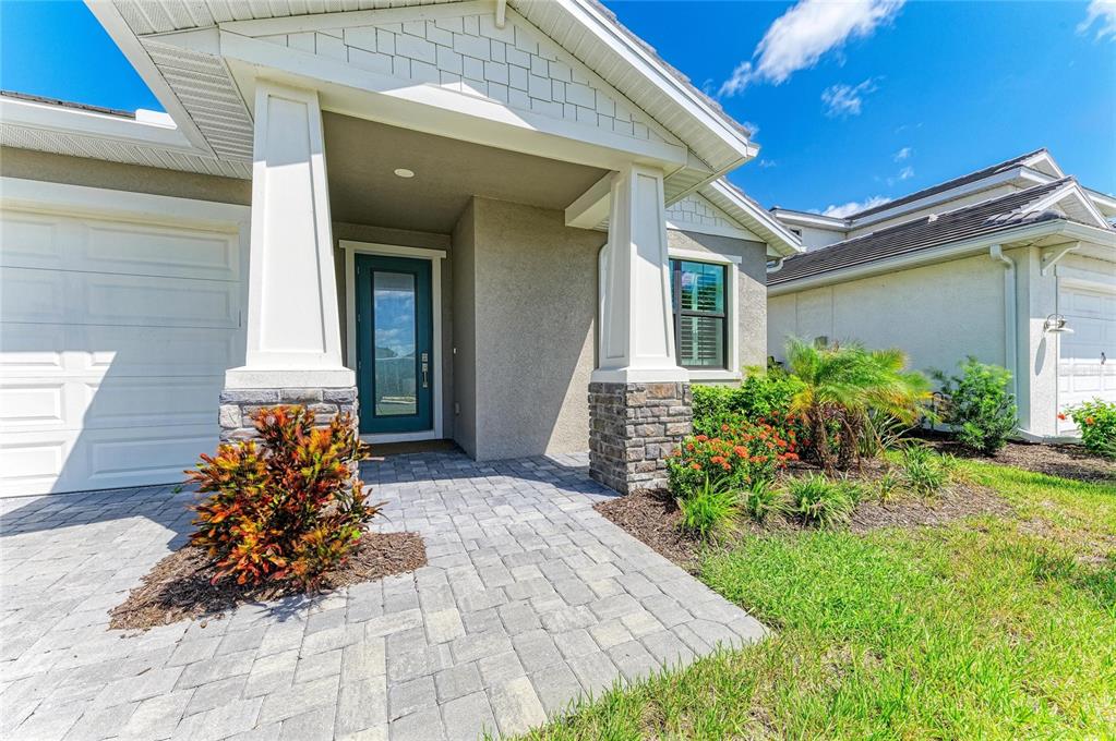 A paved walkway leads to the front entrance of a house with stone-based porch columns — 18530 MIDSUMMER PLACE, VENICE, FL