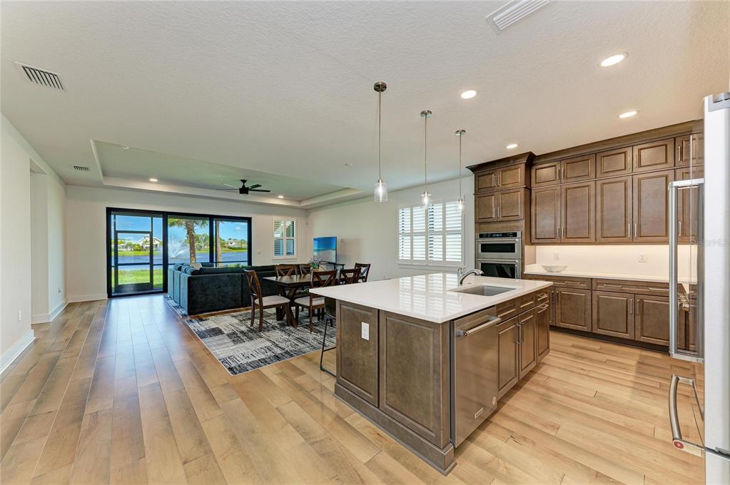An open-concept kitchen and living area featuring dark wood cabinets, a large island, and lake views — 18530 MIDSUMMER PLACE, VENICE, FL