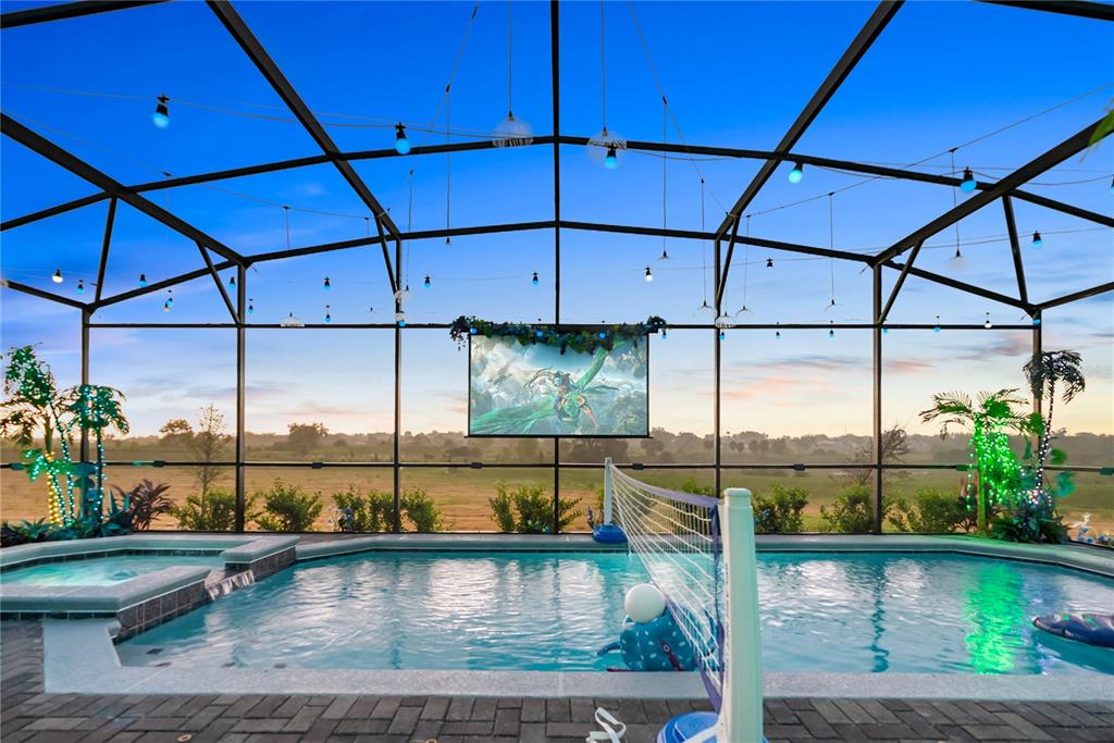 A screened-in pool area features a hot tub, volleyball net, and a large projection screen — 16016 SANDY CLIFFS DRIVE, CLERMONT, FL