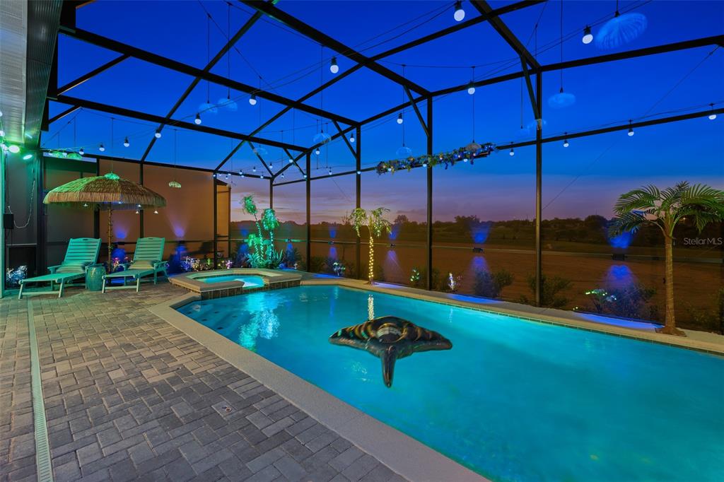 A screened-in swimming pool and hot tub area at dusk with patio furniture and lighting — 16016 SANDY CLIFFS DRIVE, CLERMONT, FL