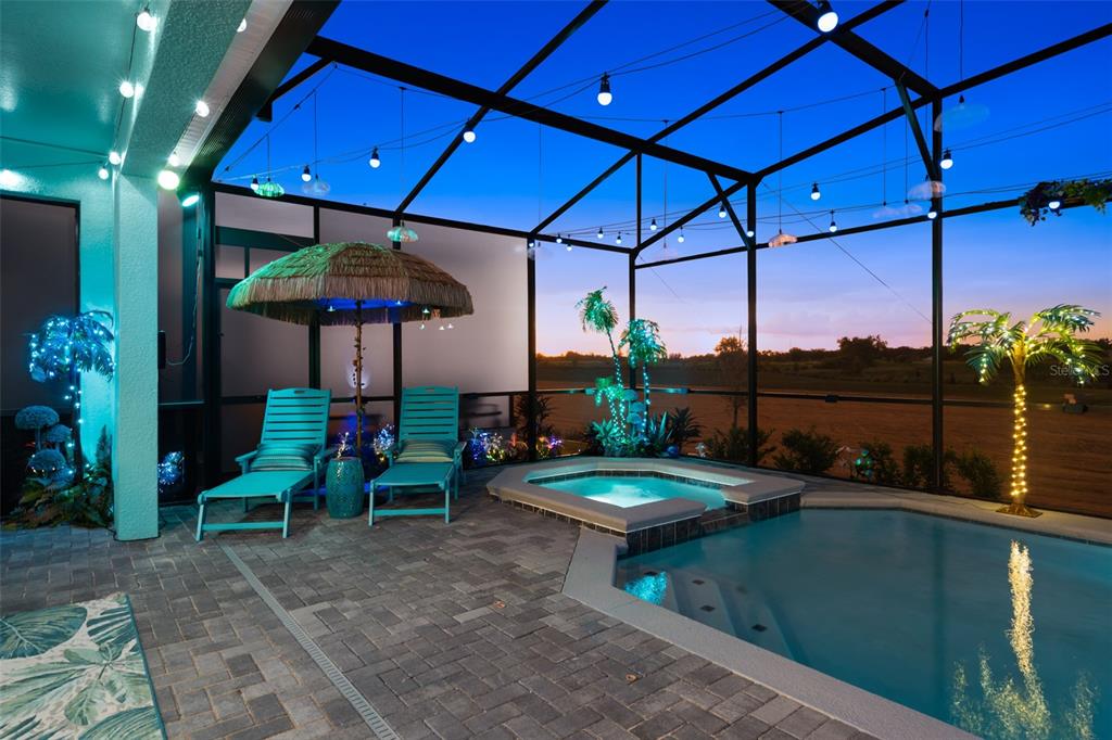 A screened-in patio features a swimming pool, a hot tub, lounge chairs, and string lights — 16016 SANDY CLIFFS DRIVE, CLERMONT, FL