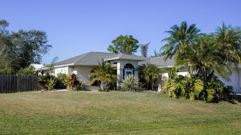 A single-story house with a light-colored exterior, a gray roof, and surrounding tropical landscaping — 3357 N CHAMBERLAIN BOULEVARD, NORTH PORT, FL