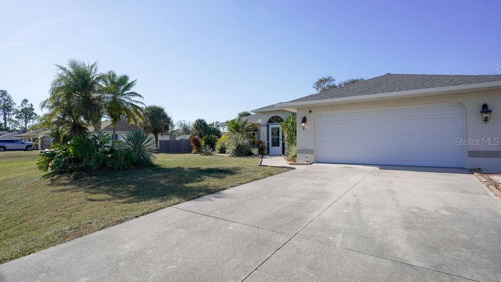A single-story house features a two-car garage, a concrete driveway, and tropical landscaping — 3357 N CHAMBERLAIN BOULEVARD, NORTH PORT, FL