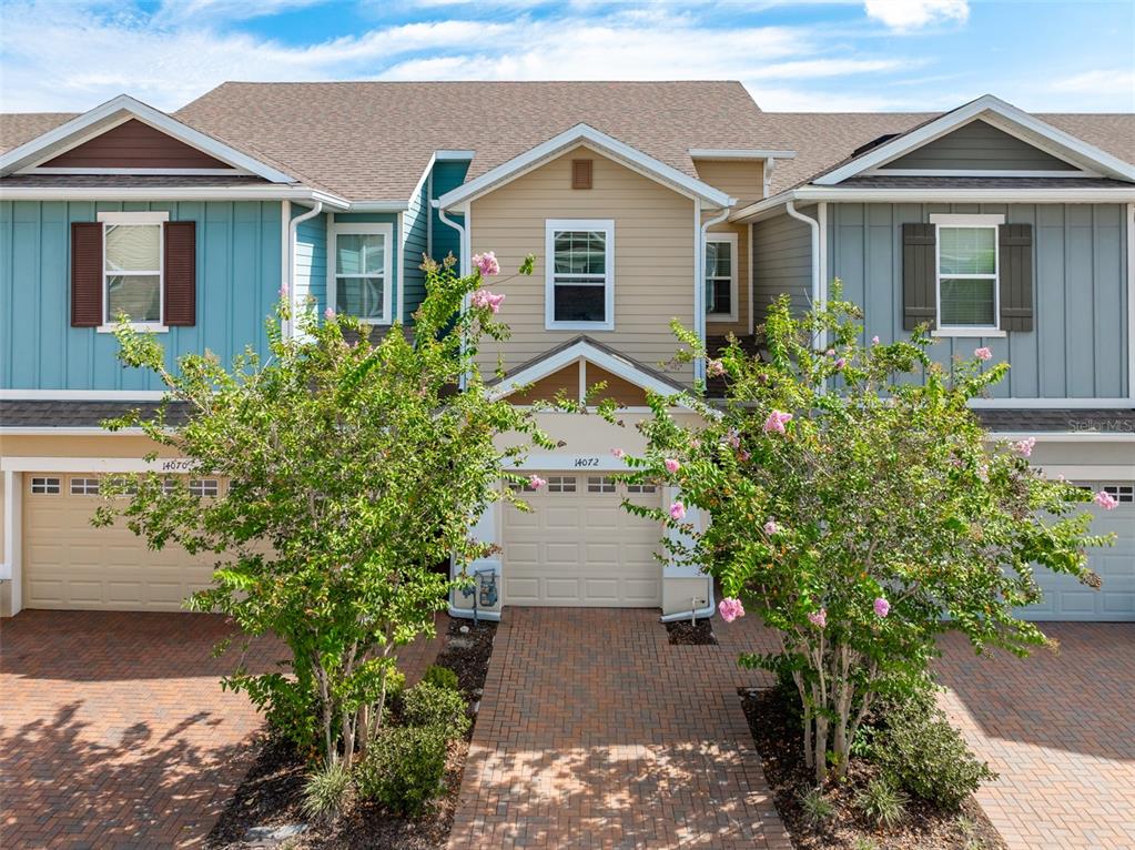 A row of three attached townhomes with tan garage doors and colorful siding under a blue sky — 14072 KITE LANE, LITHIA, FL