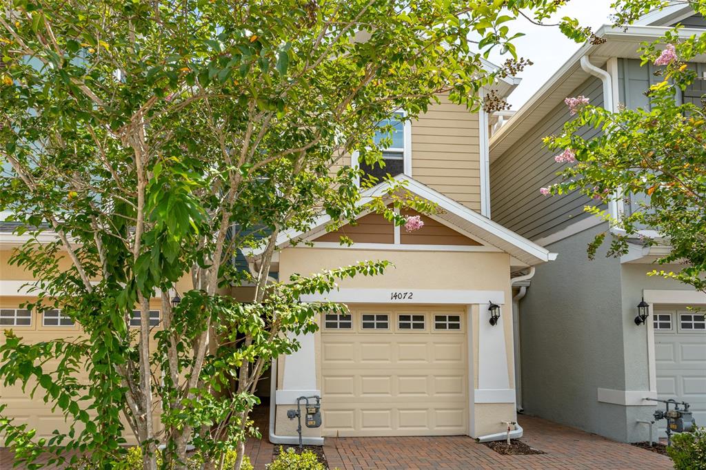 A two-story townhouse exterior features a beige garage, tan siding, and a paved driveway — 14072 KITE LANE, LITHIA, FL