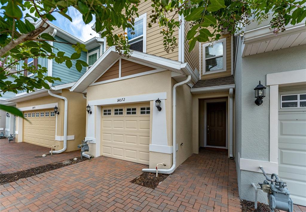 A beige two-story townhouse with a single-car garage and a brick-paved driveway — 14072 KITE LANE, LITHIA, FL