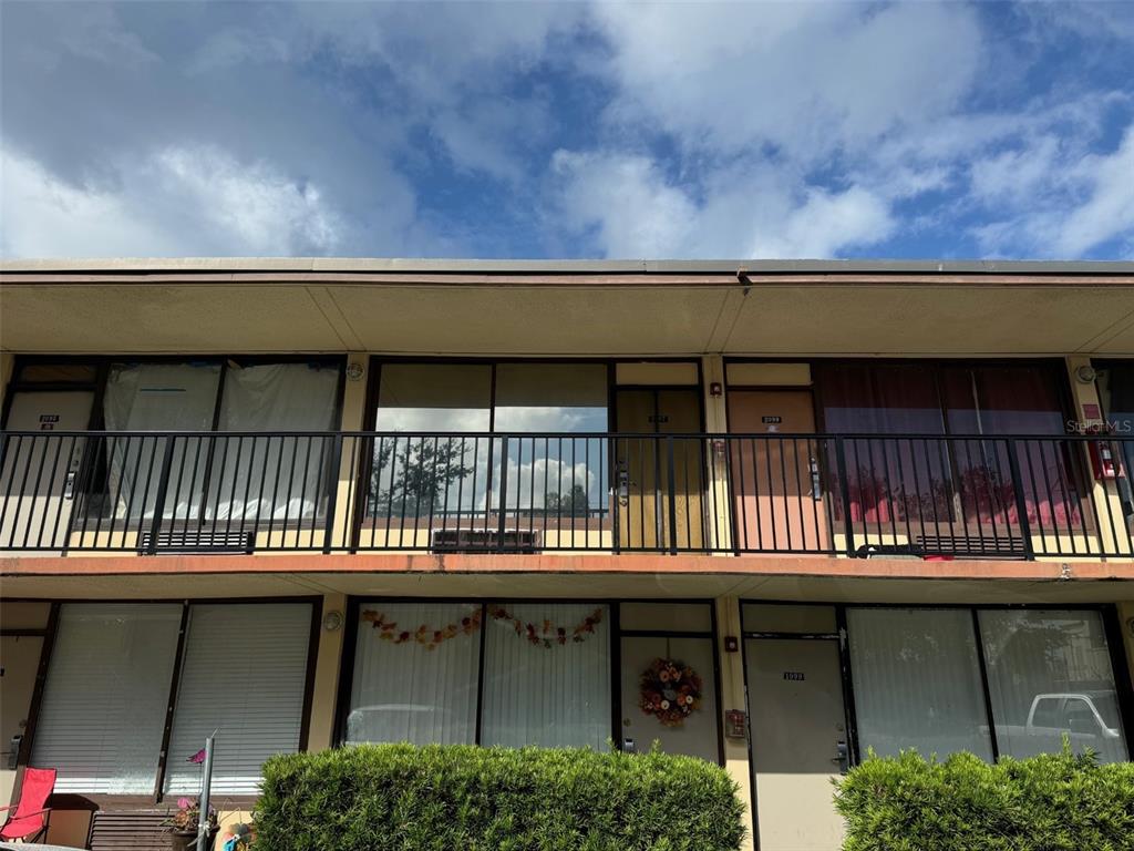 A two-story apartment building exterior features a balcony with black railings and ground-level entry doors — 7900 S ORANGE BLOSSOM TRAIL UNIT 2097, ORLANDO, FL