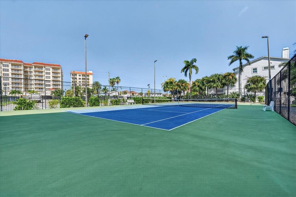A blue and green outdoor tennis court is surrounded by palm trees and a fence — 108 FOREST HILLS DRIVE, REDINGTON SHORES, FL