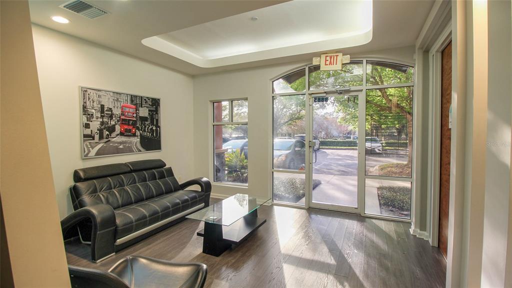 A modern office waiting area features a black leather sofa, glass coffee table, and windows — 8865 COMMODITY CIRCLE UNIT 105, ORLANDO, FL