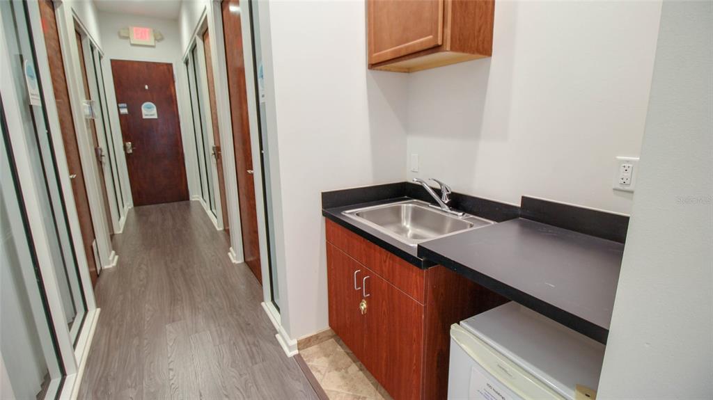 A hallway with wood-look flooring leads to a kitchenette featuring a sink and wood cabinets — 8865 COMMODITY CIRCLE UNIT 105, ORLANDO, FL