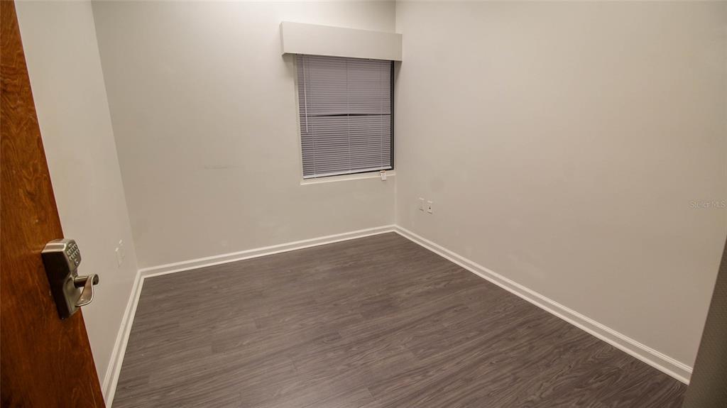 An empty room with gray wood-look flooring, white walls, and a single window with blinds — 8865 COMMODITY CIRCLE UNIT 105, ORLANDO, FL