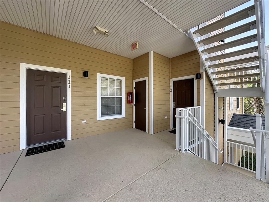 An exterior view of an apartment building entrance with two doors, stairs, and tan siding — 111 RUM RUN, DAVENPORT, FL