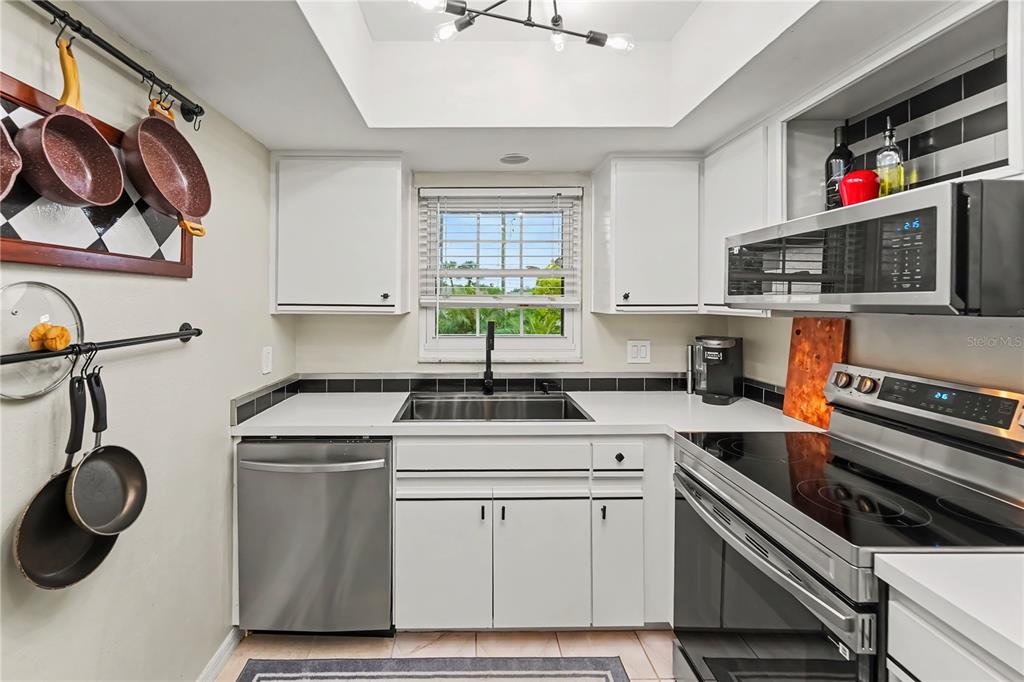 A kitchen with white cabinets, stainless steel appliances, a sink, and a window above it — 12900 VONN ROAD UNIT E204, LARGO, FL