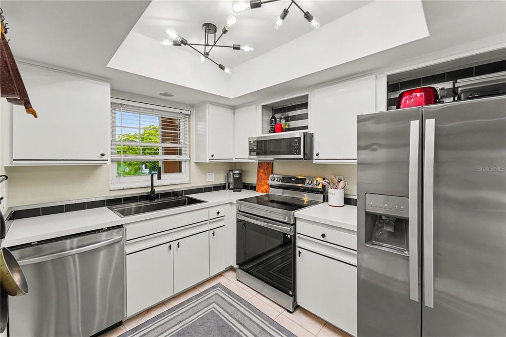 A kitchen features white cabinets, stainless steel appliances, a black backsplash, and a modern chandelier — 12900 VONN ROAD UNIT E204, LARGO, FL