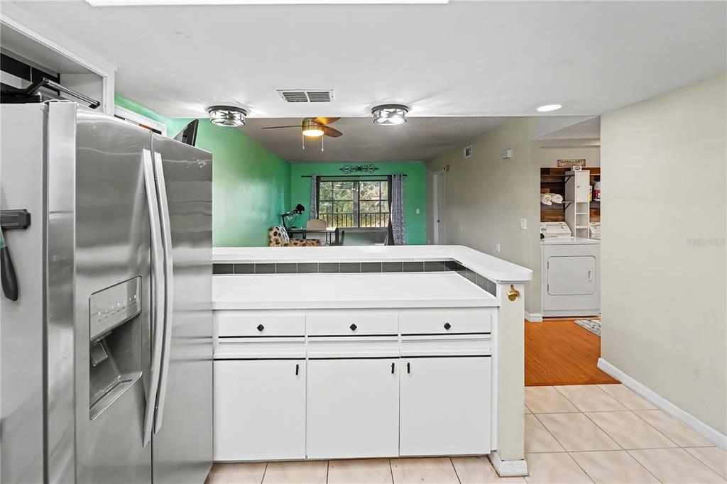 A kitchen with white cabinets and a stainless steel refrigerator overlooks a green-walled living area — 12900 VONN ROAD UNIT E204, LARGO, FL