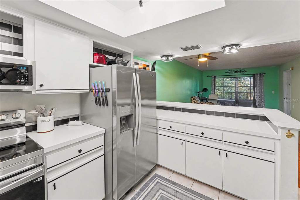 A kitchen with white cabinets and stainless steel appliances overlooks a green-walled living area — 12900 VONN ROAD UNIT E204, LARGO, FL