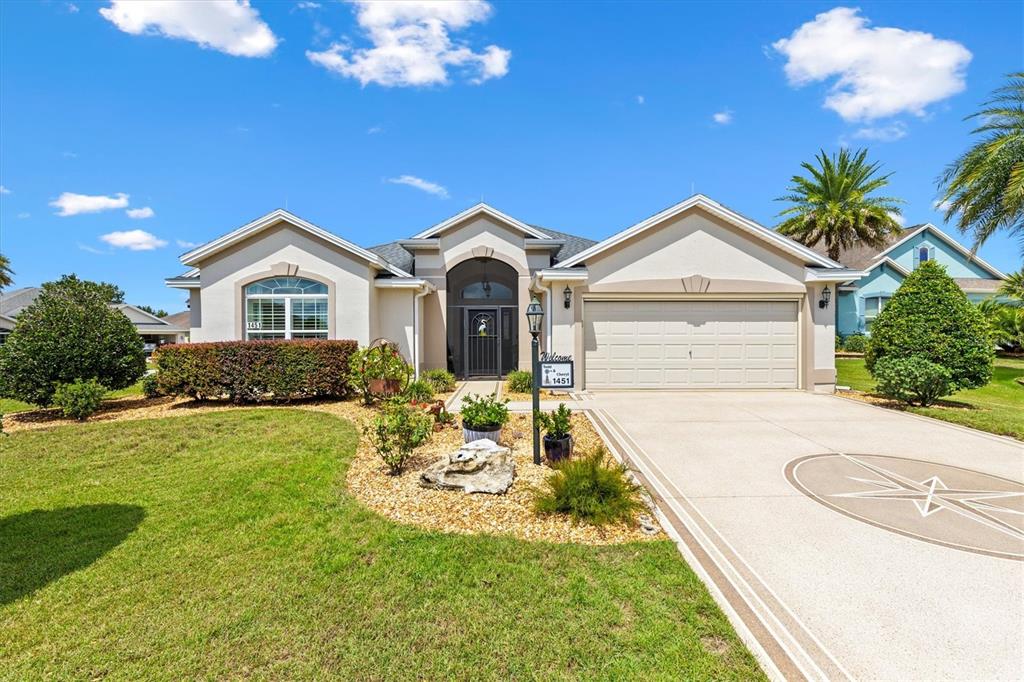 A single-story suburban house with a beige stucco exterior, a two-car garage, and landscaping — 1451 LUCKETT COURT, THE VILLAGES, FL