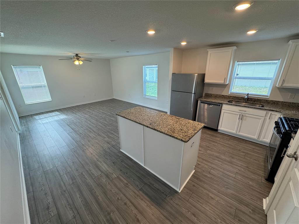 An open-concept kitchen and living area features gray wood-look flooring, white cabinets, and granite countertops — 233 KENSINGTON VIEW BOULEVARD, WINTER HAVEN, FL