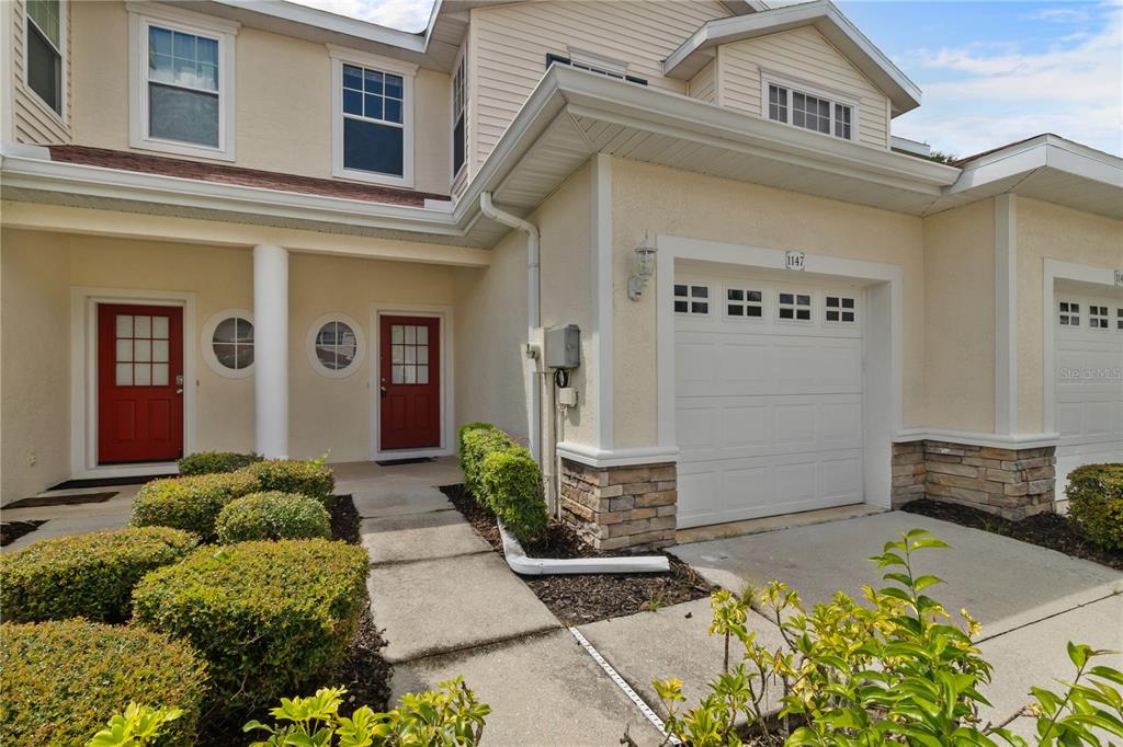 A two-story townhouse exterior features two red front doors, a garage, and manicured landscaping — 1147 JONAH DRIVE, NORTH PORT, FL